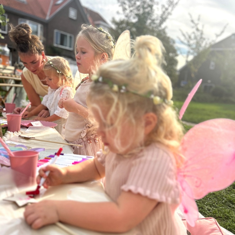 Kinderen met feeënvleugels aan de tafel, midden in een opdracht, Jolie helpt mee
