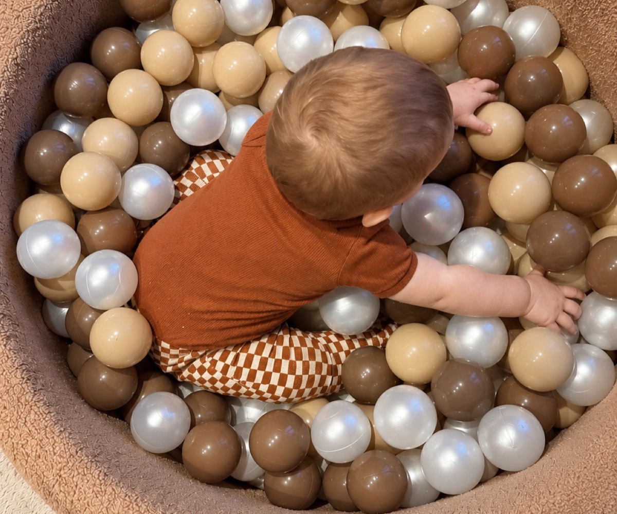Klein kind zit in de ballenbak en graait met twee handen door de ballen