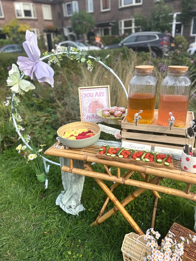 Het drankstation met twee tapkannen limonade, fruit en cupcakes achter een bloemenhoepel
