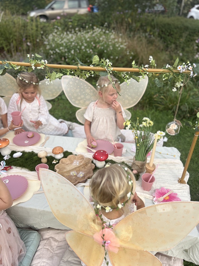 Twee kinderen met feeënvleugels en bloemenkransjes aan tafel