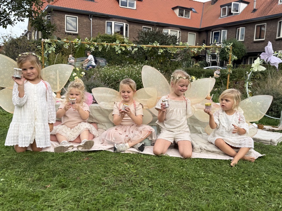De hele groep feeën op een rij op een kleed in het gras, elk met een eigen feeënpotje