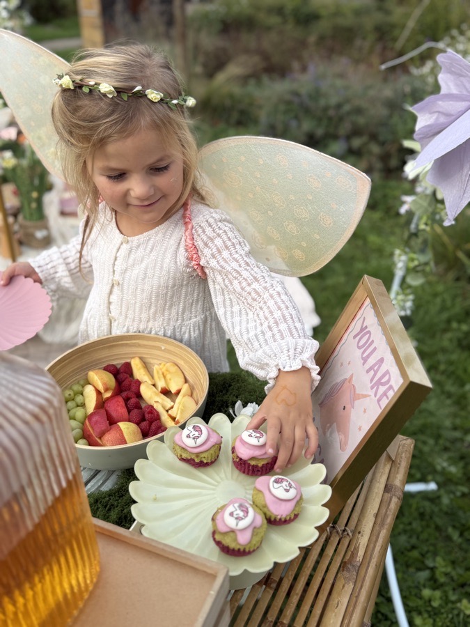 Meisje met vleugels pakt een cupcake van de taartstandaard