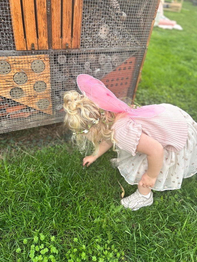 Meisje met roze vleugels bukt zich bij het insectenhotel, op zoek naar de unicorns