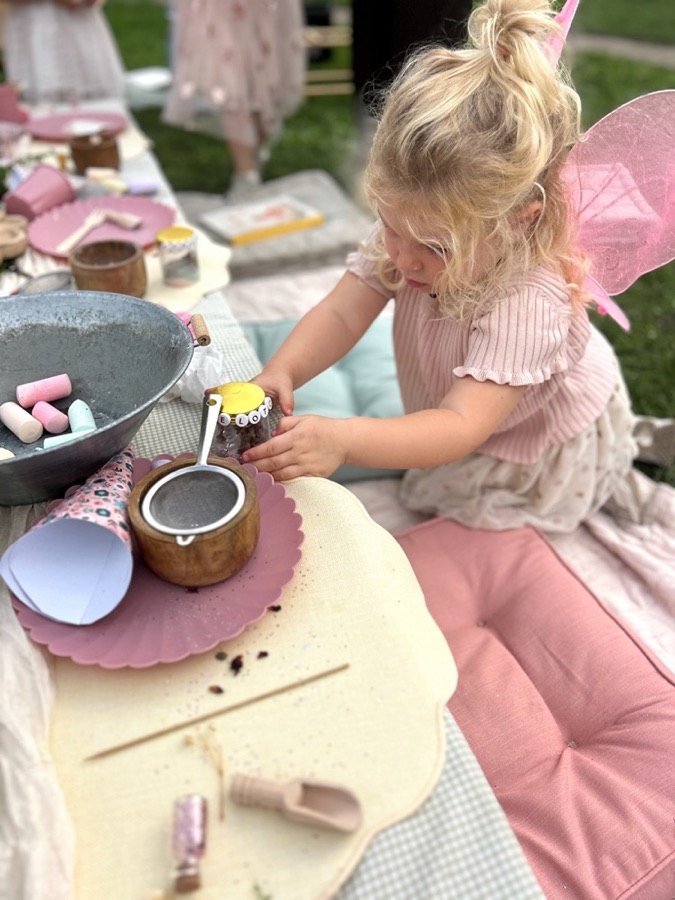 Meisje roert haar eigen fairy jar bij elkaar aan de picknicktafel