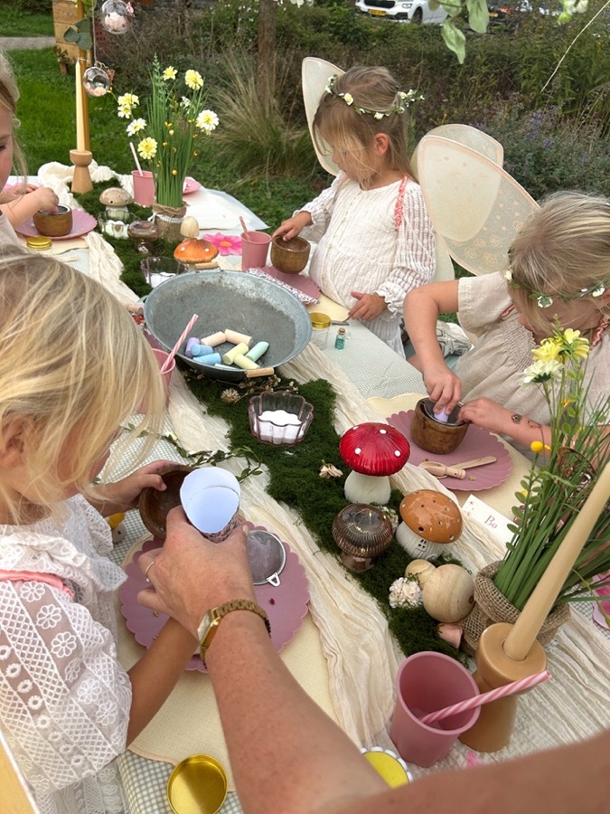 Van bovenaf: de kinderen vullen hun fairy jars aan de lange tafel